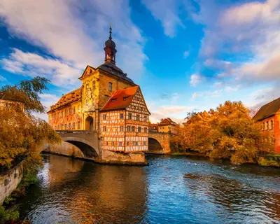 Autumn scenery with Old Town Hall in the middle of rapid river under moving picturesque clouds at sunny day. Bamberg, Germany. UNESCO World Heritage Site.