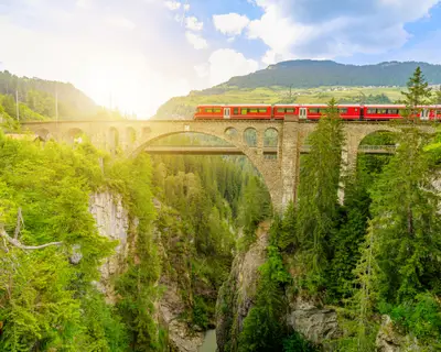Red train crossing the Solis Viaduct bridge of Swiss railway in Switzerland to Pontresina town. Swiss train Bernina in Grisons at sunset. Albula Railway section between Thusis and Tiefencastel
