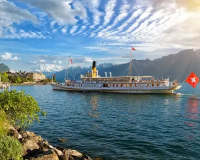 Beautiful summer evening landscape of Lake Geneva with picturesque shores and pleasure ship against Alpine mountains in the rays of the setting sun in Montreux, Switzerland