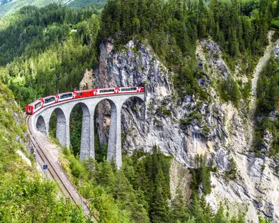 Landscape with Landwasser Viaduct in summer, Filisur, Switzerland. It is landmark of Swiss Alps. Panoramic view of railroad bridge and red train. Rhaetian glacier express runs on amazing railway.