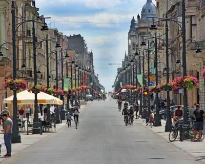 View of city street with many flowers and people riding bicycles. City life in Lodz. Central street of Lodz Piotrkowska street. Beautiful urban panorama. Urban life. Panoramic urban view