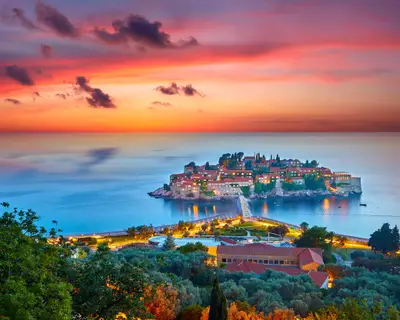 Amaizing sunset view on Sveti Stefan Island City. Small islet and resort in Montenegro. Balkans, Adriatic sea, Europe. Dramatic red sky under a Saint Stefan peninsula.